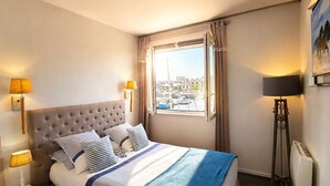 Une chambre d’hôtel avec un lit, deux lampes de chevet, une fenêtre avec des rideaux, un radiateur et un tableau au mur.