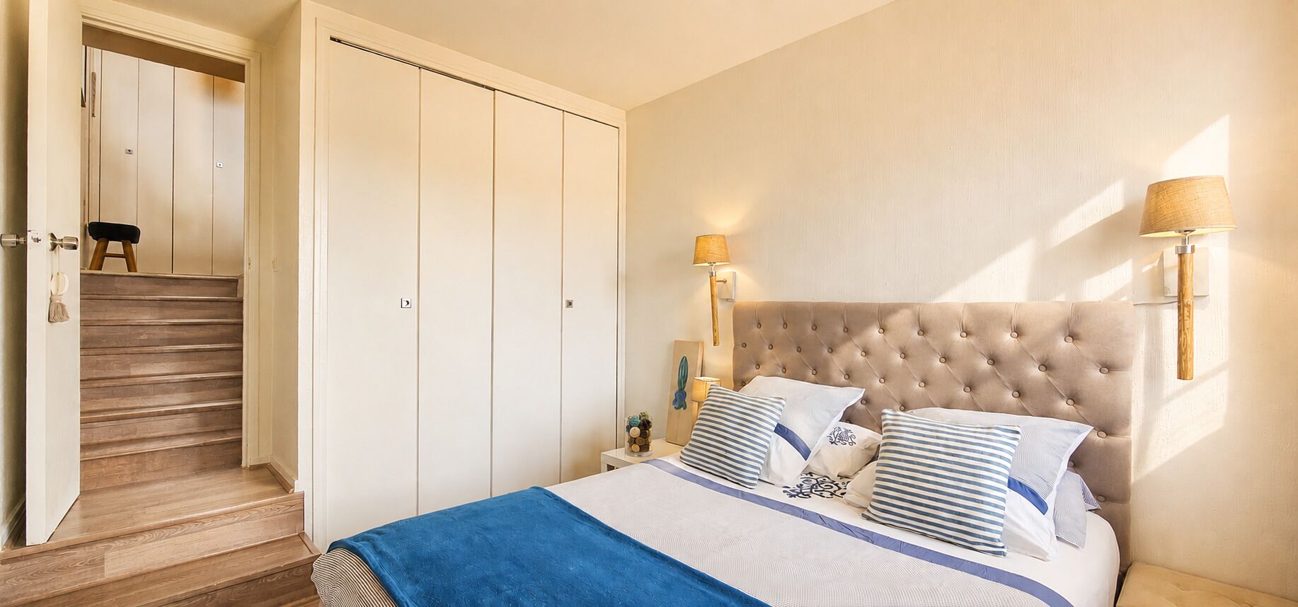 A bedroom with a bed, a nightstand, a lamp, a wardrobe, and a staircase.