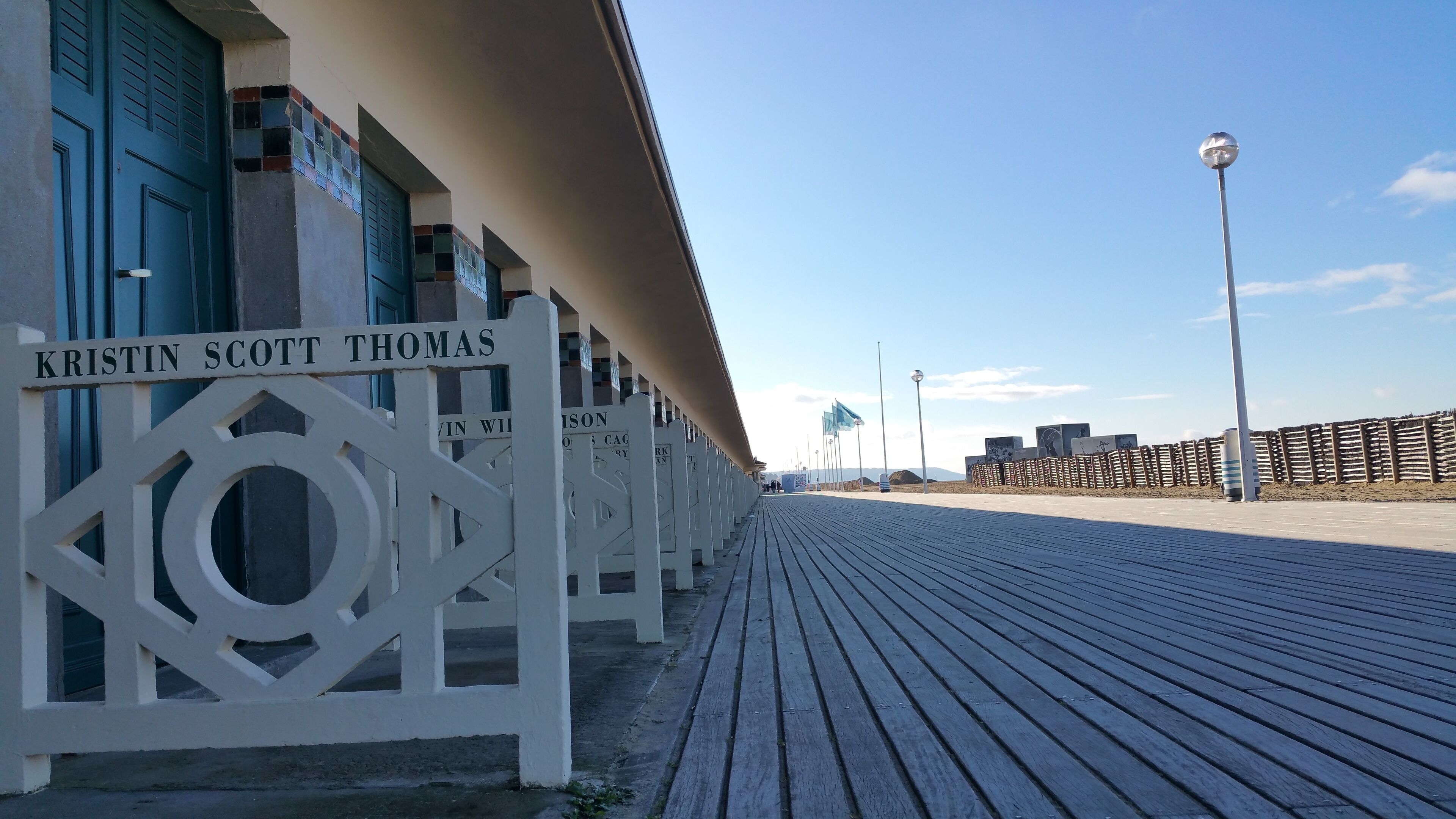 En træpromenade med hvide dekorative stolper, hvoraf nogle har navne som 'KRISTIN SCOTT THOMAS'.
