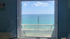 Quarto com vista para o mar através de uma janela aberta, grade de varanda e radiador.