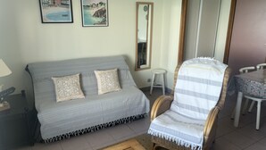 Uma sala de estar com um sofá cinzento, uma poltrona de vime, uma mesinha e duas imagens emolduradas na parede.