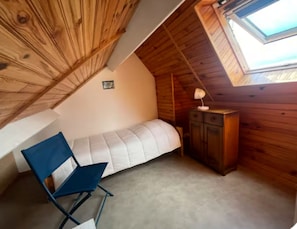 A small, cozy attic bedroom with a slanted ceiling, a single bed, a desk, a chair, and a small cabinet. - Apartment 180° sea view direct beach access (Fouesnant)