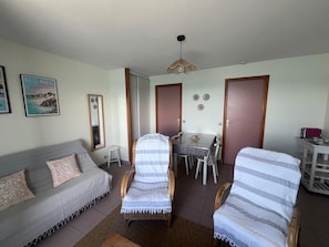 A living room with a sofa, two striped armchairs, a dining table with chairs, a hanging light fixture, and a mirror. - Apartment 180° sea view direct beach access (Fouesnant)