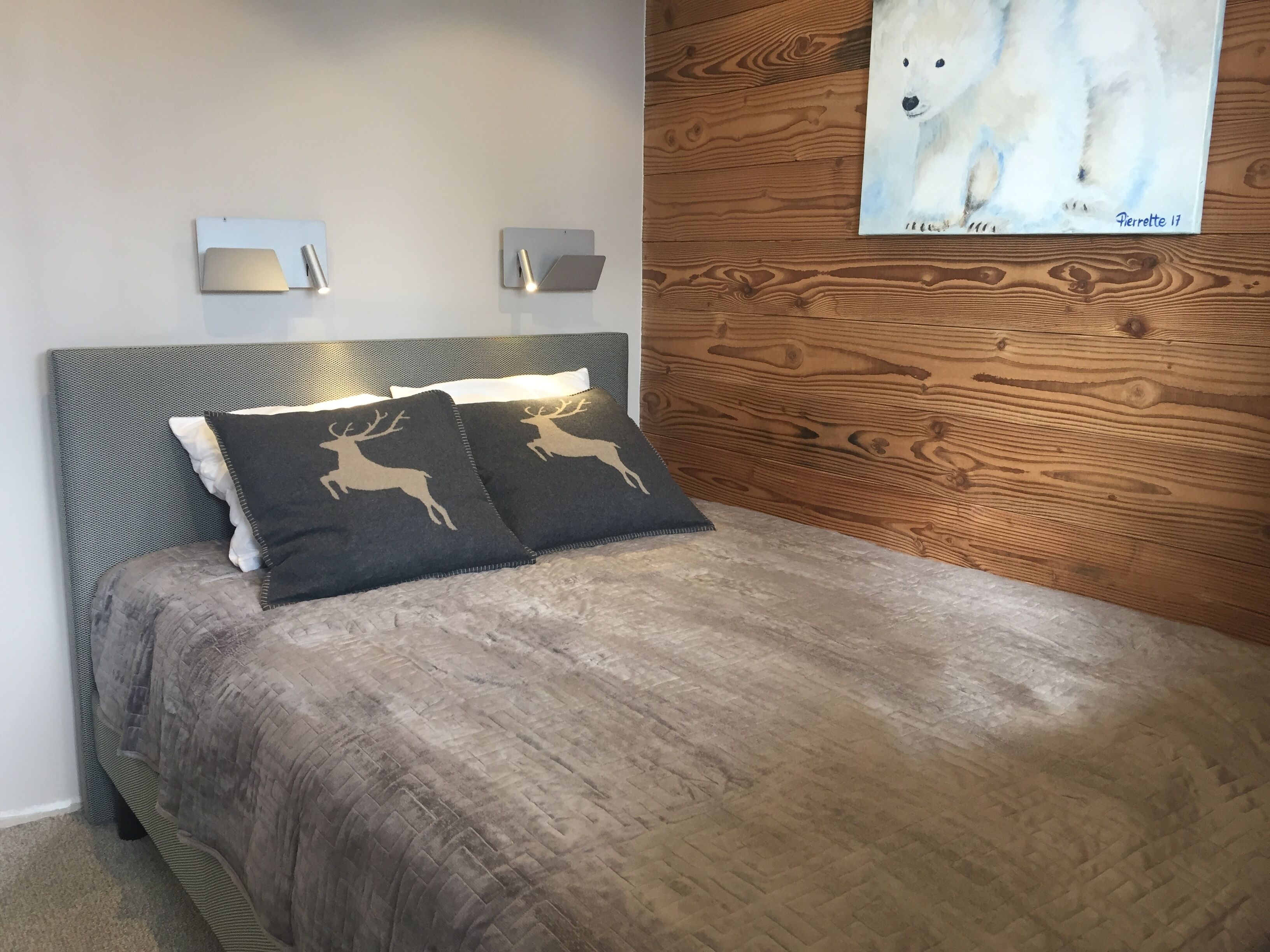 A bedroom with a bed, two wall-mounted light fixtures, and a wooden panel wall with a painting.