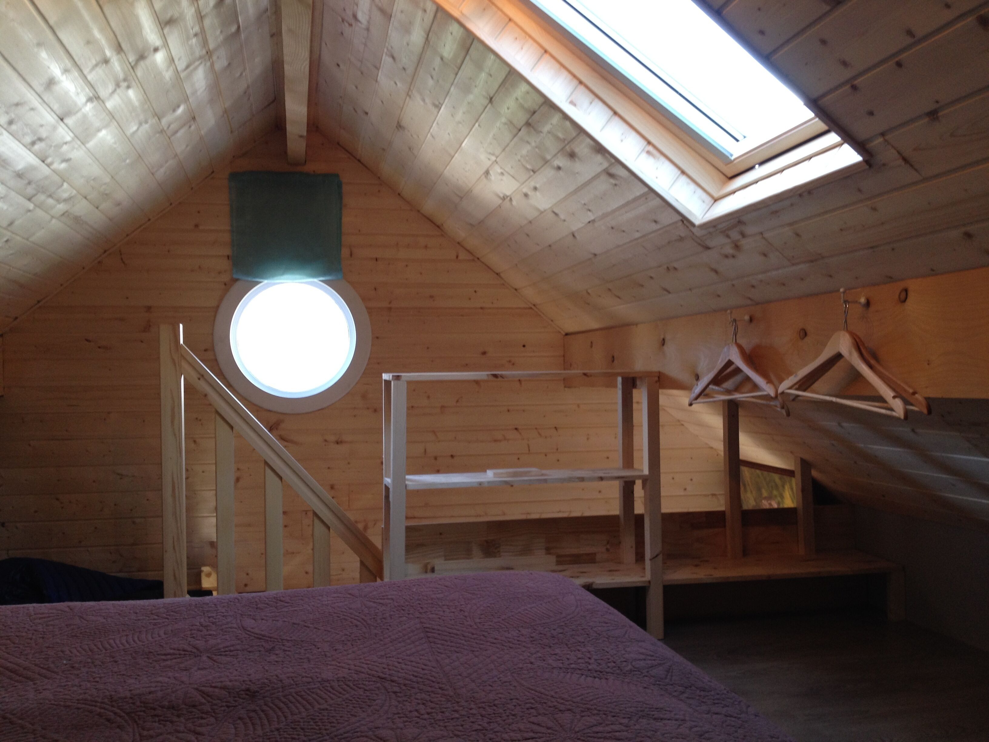 Ein Schlafzimmer im Dachgeschoss mit hohen Decken, einem Dachfenster, Holzbalken und einem Etagenbett.