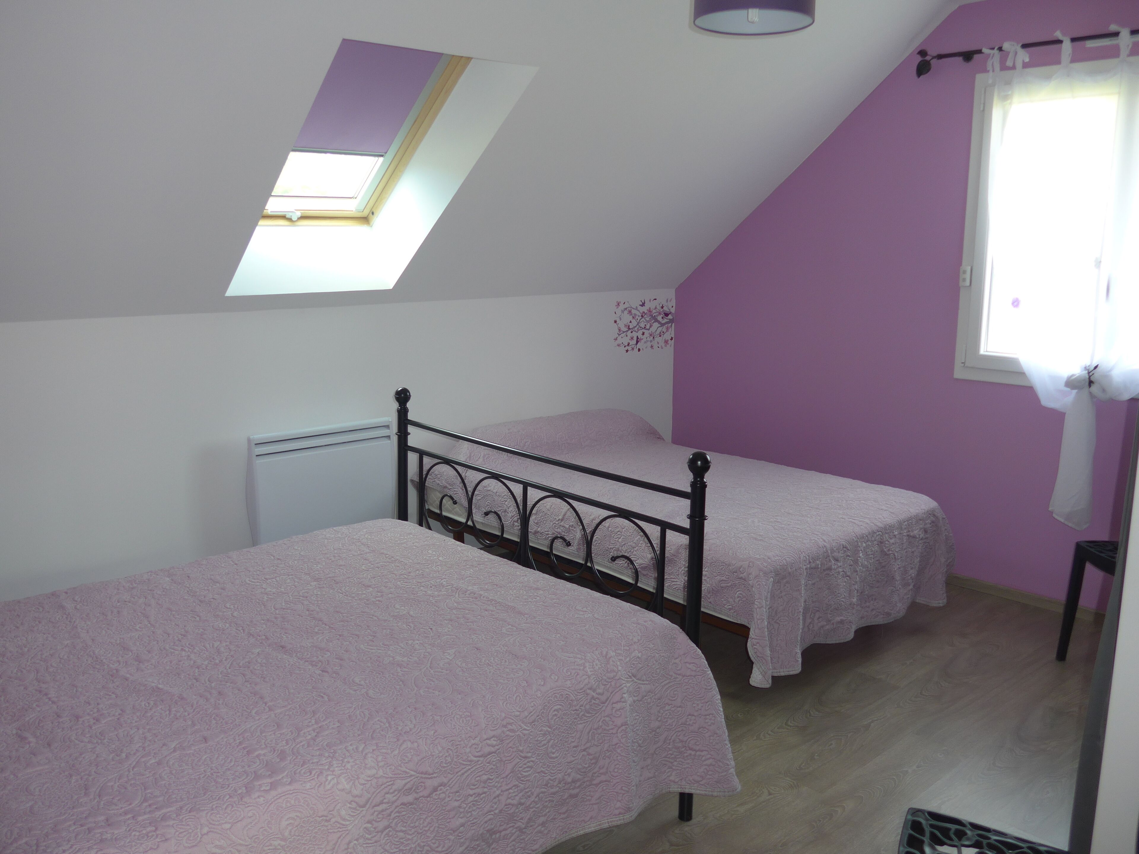 Een slaapkamer met twee enkele bedden, een dakraam, een radiator en een raam met gordijnen.