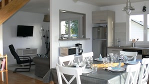 A dining area with a table set for four, a television mounted on the wall, and a kitchen area with a refrigerator and microwave. - HOUSE LOCTUDY Pays Bigouden, 3 bedrooms, Beach 600m, Expo South. Bikes. Wifi (Loctudy)