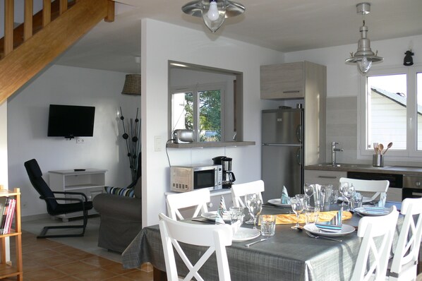 A dining area with a table set for four, a television mounted on the wall, and a kitchen area with a refrigerator and microwave.