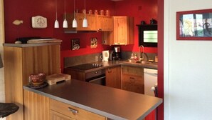 Una cocina compacta con gabinetes de madera, encimera de acero inoxidable, lámparas colgantes y horno empotrado.
