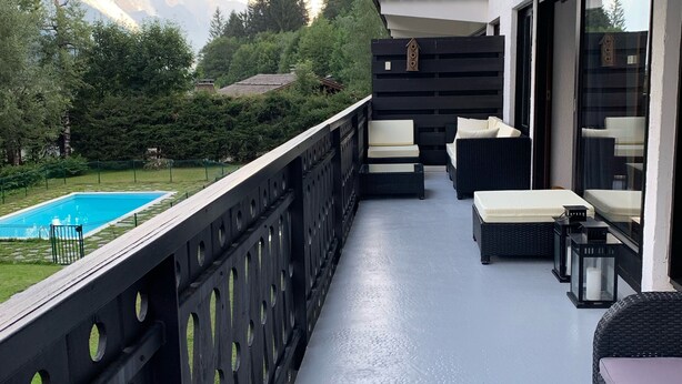 Un balcón con piscina, mobiliario exterior y vistas a montañas.