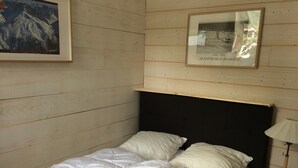 Una cama con ropa de cama blanca, cabecera negra y un cuadro enmarcado con una escena de montaña en la pared.