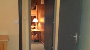 Un couloir avec une porte en bois, une petite table avec une lampe et un tapis à motifs.