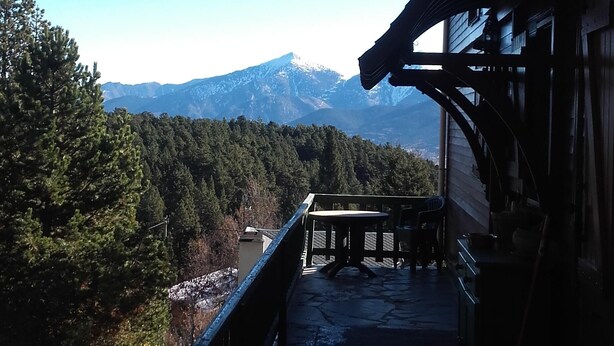 Un bâtiment en bois doté d’un balcon dallé de pierres, qui offre une vue sur une vallée boisée et sur des montagnes lointaines.