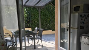 Una cocina moderna con refrigerador, microondas y armarios. Hay un comedor con una mesa y sillas, y un vidrio que da a un patio exterior con mesa y sillas.