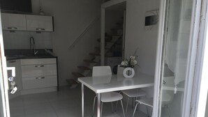 Una cocina moderna con armarios blancos, un lavamanos de acero inoxidable y una escalera que sube al piso superior.