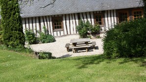 Une maison traditionnelle à colombages, dotée d’une terrasse en gravier et d’un banc en bois.
