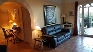 Una sala de estar con un sofá de cuero negro, una mesa de comedor con una laptop, una lámpara y un cuadro de un tigre en la pared.