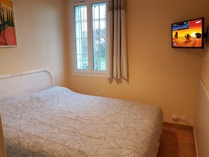 Un dormitorio con cama, ventana con cortinas, televisor en la pared y un cuadro en la pared.