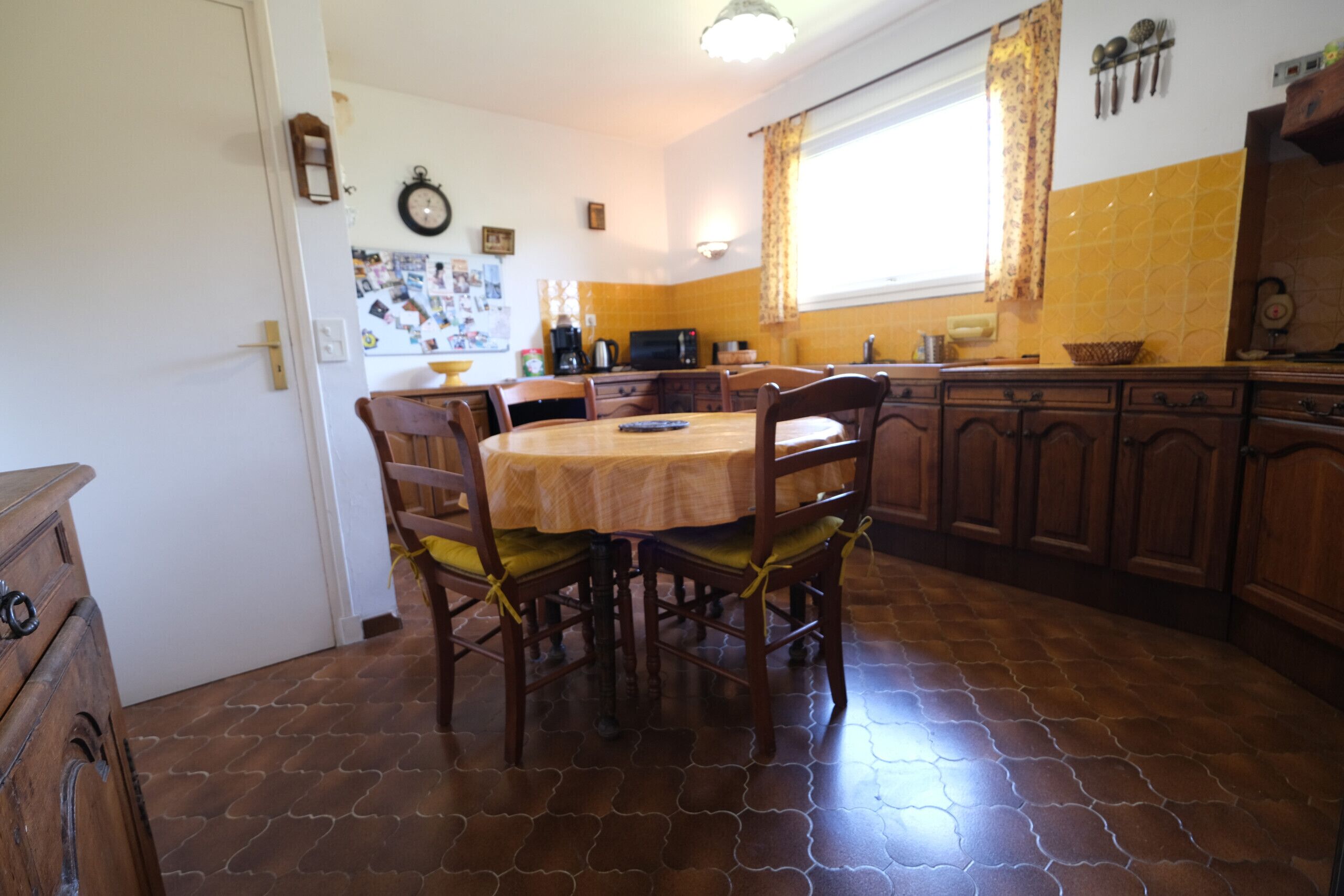 Un comedor con una mesa redonda y sillas, una cocina con armarios de madera y un suelo de baldosas.