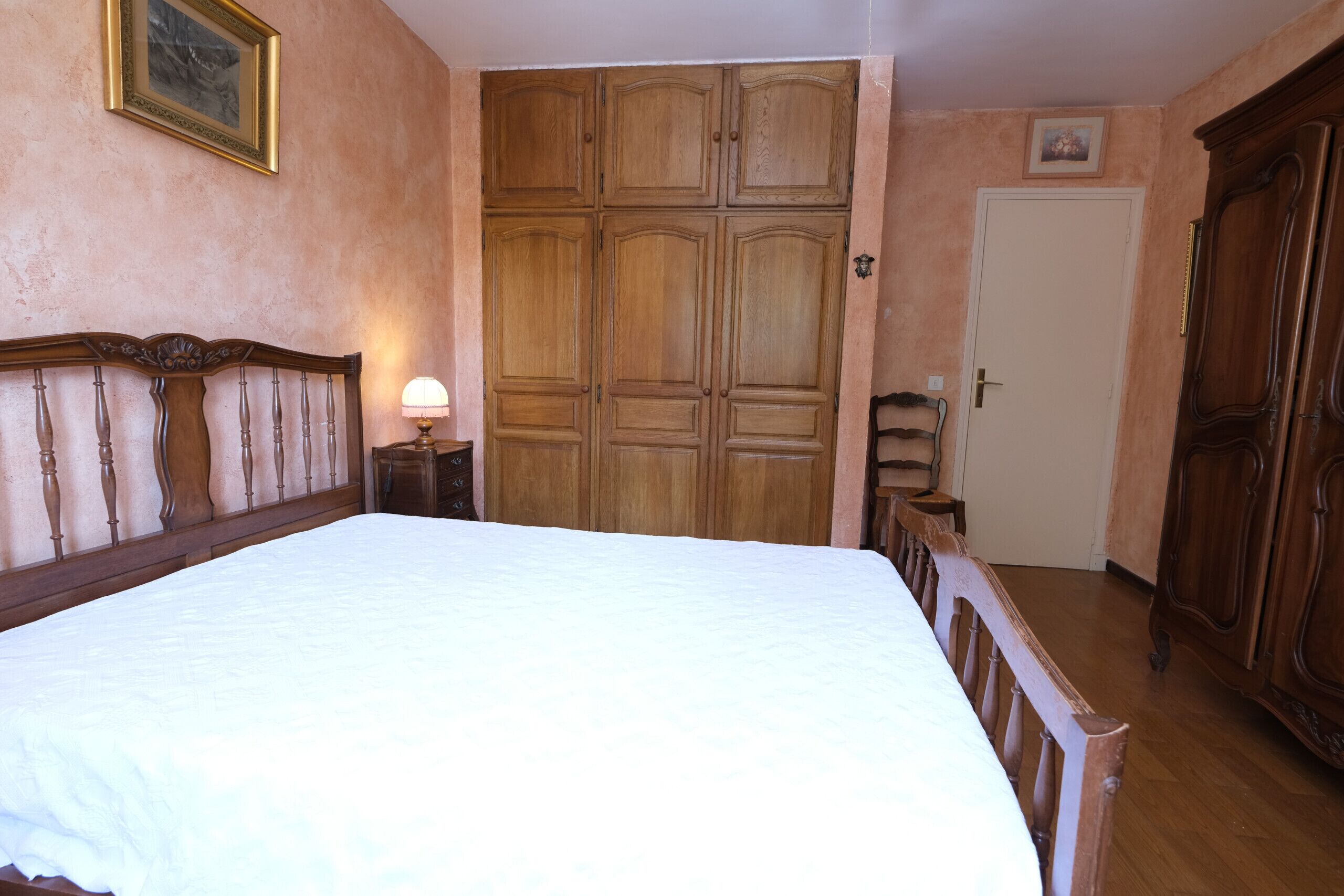 A bedroom with a large bed, wooden wardrobe, and a door.