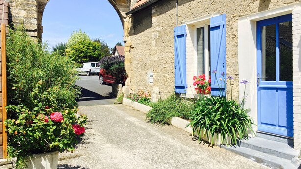 Una estrecha calle con un arco de piedra, un edificio con contraventanas azules y un coche estacionado.