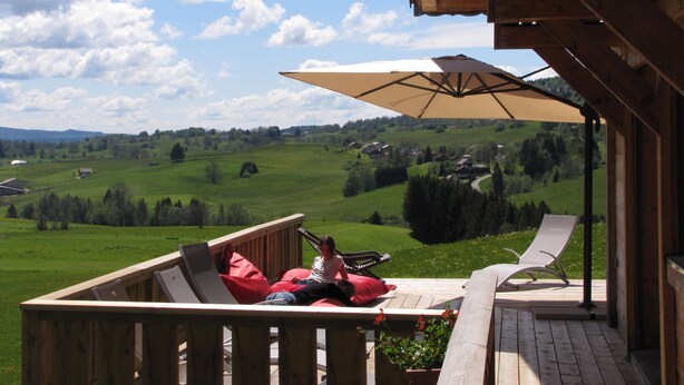 Eine Holzterrasse mit Blick auf ein grünes Tal und Häuser.