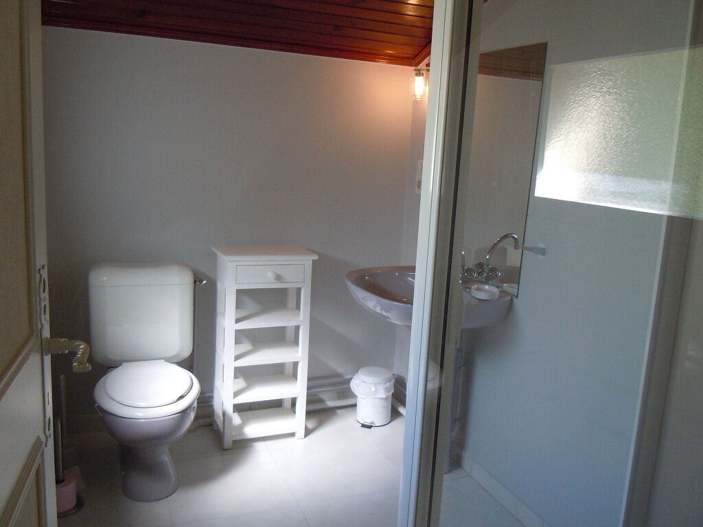 Une petite salle de bain compacte, équipée de toilettes, d’une étagère blanche et d’un lavabo.