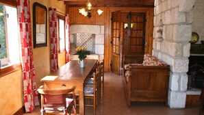 A wooden interior with a long dining table, chairs, a bench, and a stone wall.