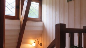 Een houten trap met een leuning, een klein raam en een wandlamp.