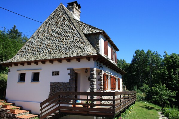A traditional stone house with a steeply pitched roof, wooden balcony, and a stone staircase leading to the entrance.