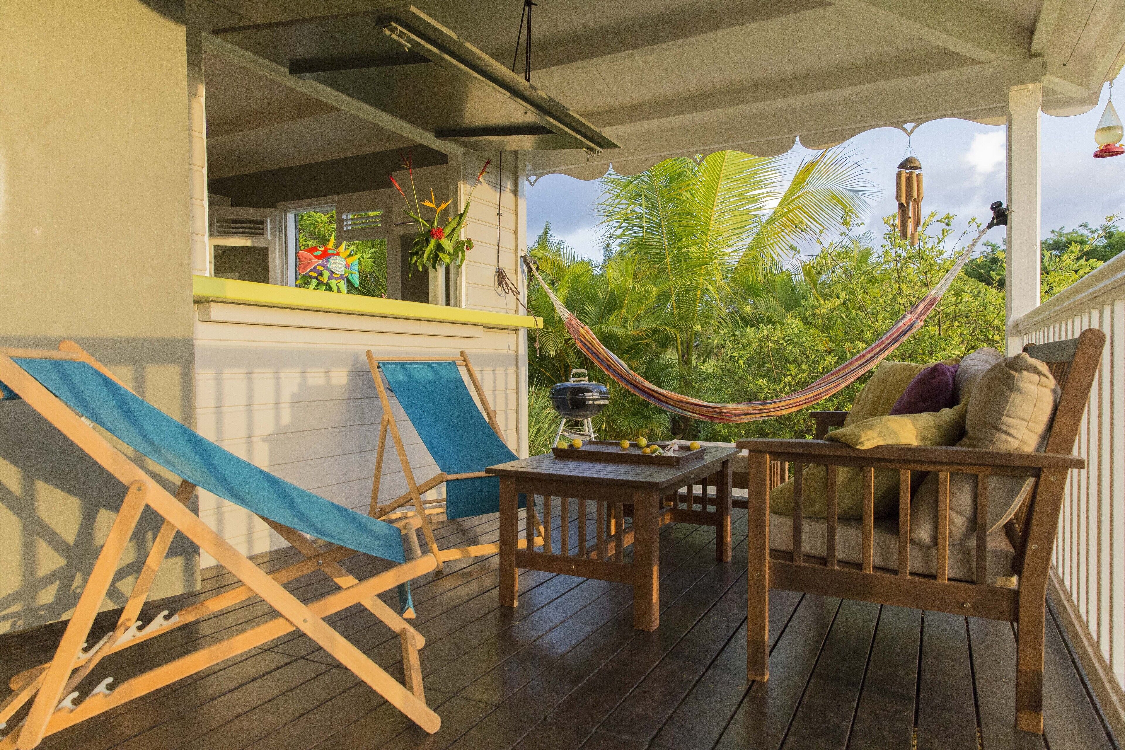 A wooden deck with a hammock, a table with a grill, and a chair.