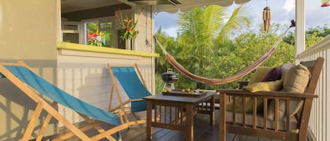 A wooden deck with a hammock, a table with a grill, and a chair.