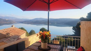 Un balcón con una sombrilla roja, una planta en maceta y vistas a un lago y montañas.