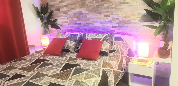 Una cama con ropa de cama estampada y almohadas rojas, cabecera con diseño de ladrillos y dos lámparas de noche.