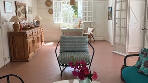 A spacious room with a large window, a wooden cabinet, a wicker pendant light, a glass coffee table with a bowl, and a teal sofa. - Large family home with private beach  (Sainte Anne)