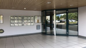 Een moderne gevel met houten plafond, glazen deur en prikbord met brievenbussen.