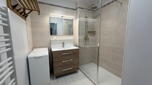 Ein modernes Badezimmer mit einer gläsernen Duschkabine, einem weißen Waschbecken mit Spiegel darüber und einer Holzausstattung mit Schubladen.