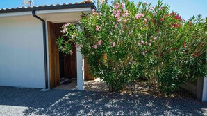 Ein Gebäude mit einem Schotterweg, einer Holztür und einem Busch mit rosa Blüten.
