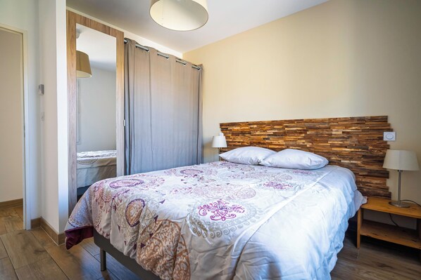 Un dormitorio con cama, cabecera de madera, dos lámparas de noche y suelo de madera.