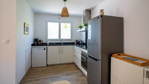 Eine moderne Küche mit weißen Schränken, einem Edelstahlkühlschrank, einer Holz Arbeitsplatte und einem Fenster mit Tageslicht.