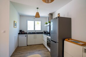 A modern kitchen with white cabinets, a stainless steel refrigerator, a wooden countertop, and a window with natural light.