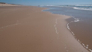 Ein weiter Sandstrand mit sanften Wellen und blauem Himmel.