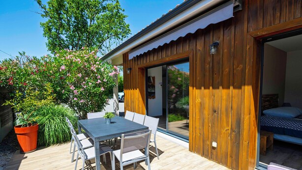 Eine Holzterrasse mit Tisch, Stühlen, einem Blumentopf und einer Glastür, die zu einem Schlafzimmer führt.
