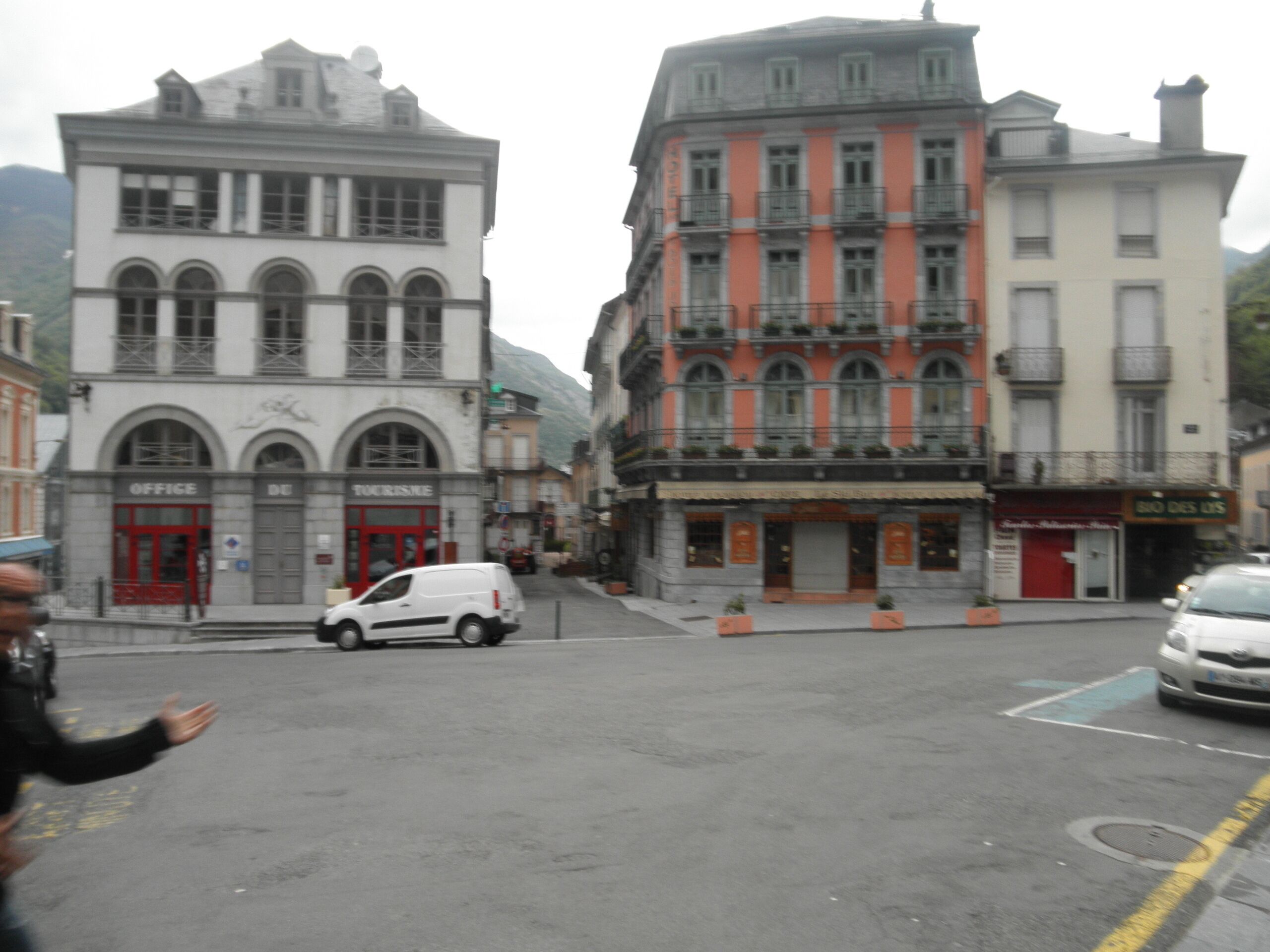 A street with buildings, including a white building with a red door labeled "TOURISM" and a multi-story building with balconies.
