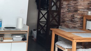 A room with a wooden dining table, a white cabinet, a wall clock, and a ceiling fan. - rent studio center of the village 2 people (Cauterets)
