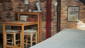 A bedroom with a sloped ceiling, a bed, a desk with chairs, and a stone wall. - rent studio center of the village 2 people (Cauterets)