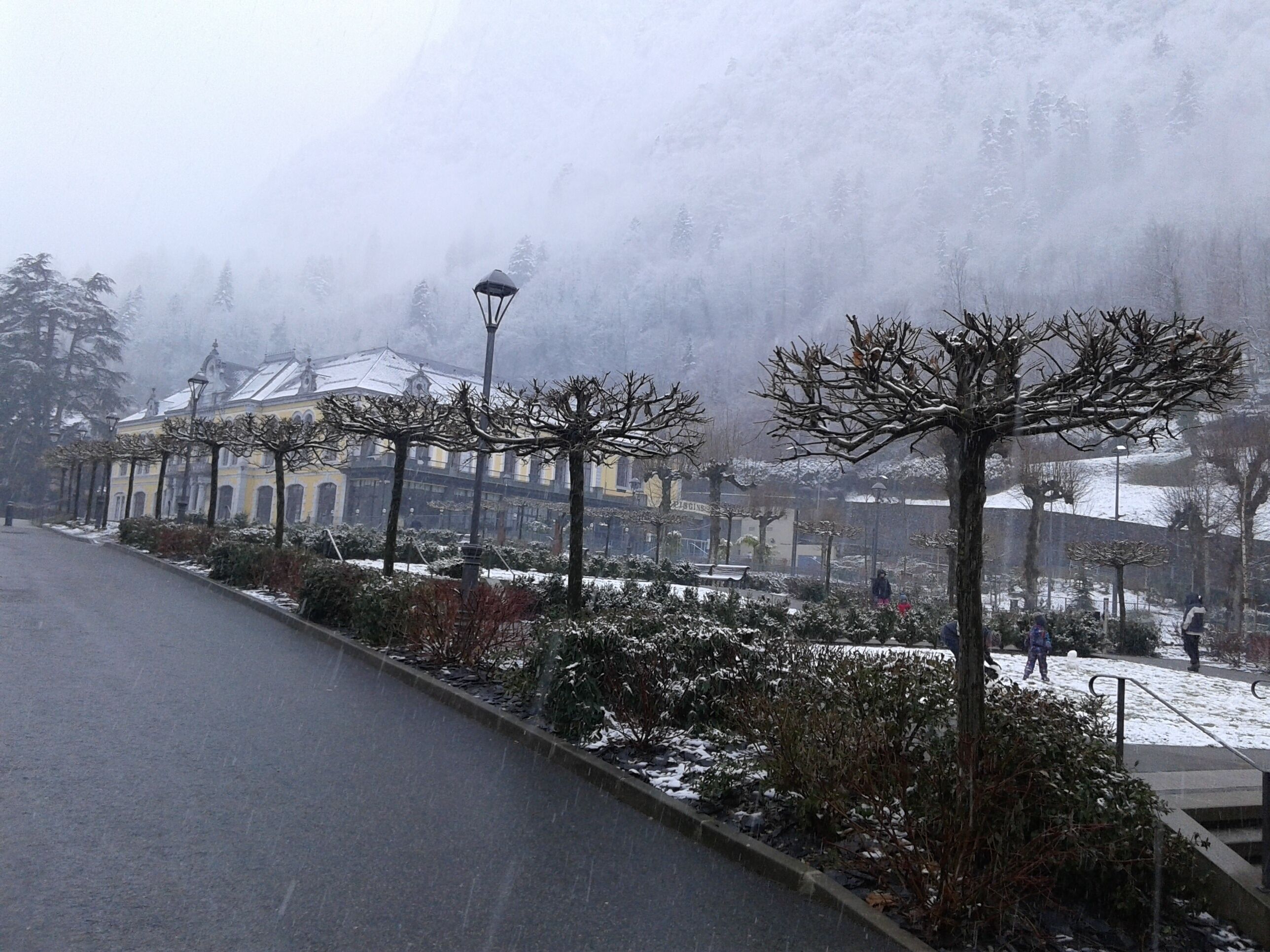 A snow-covered street with a building featuring arched windows and a snow-covered roof.