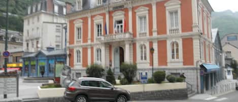 Ein historisches Gebäude mit klassischer Architektur, ein geparktes Auto davor und eine Fußgängerüberweg.
