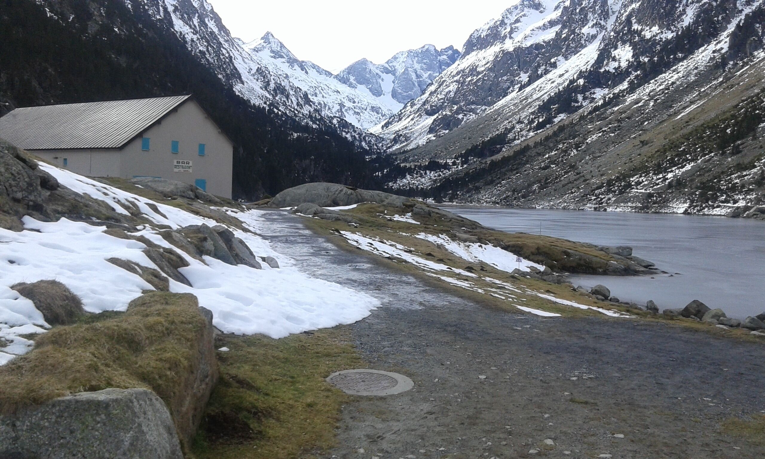 A mountain lodge with a bar, a road leading to a lake, and snow-covered mountains.