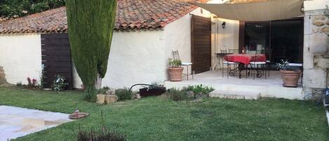 A courtyard with a neatly trimmed hedge, a patio with outdoor furniture, and a building with a tiled roof.